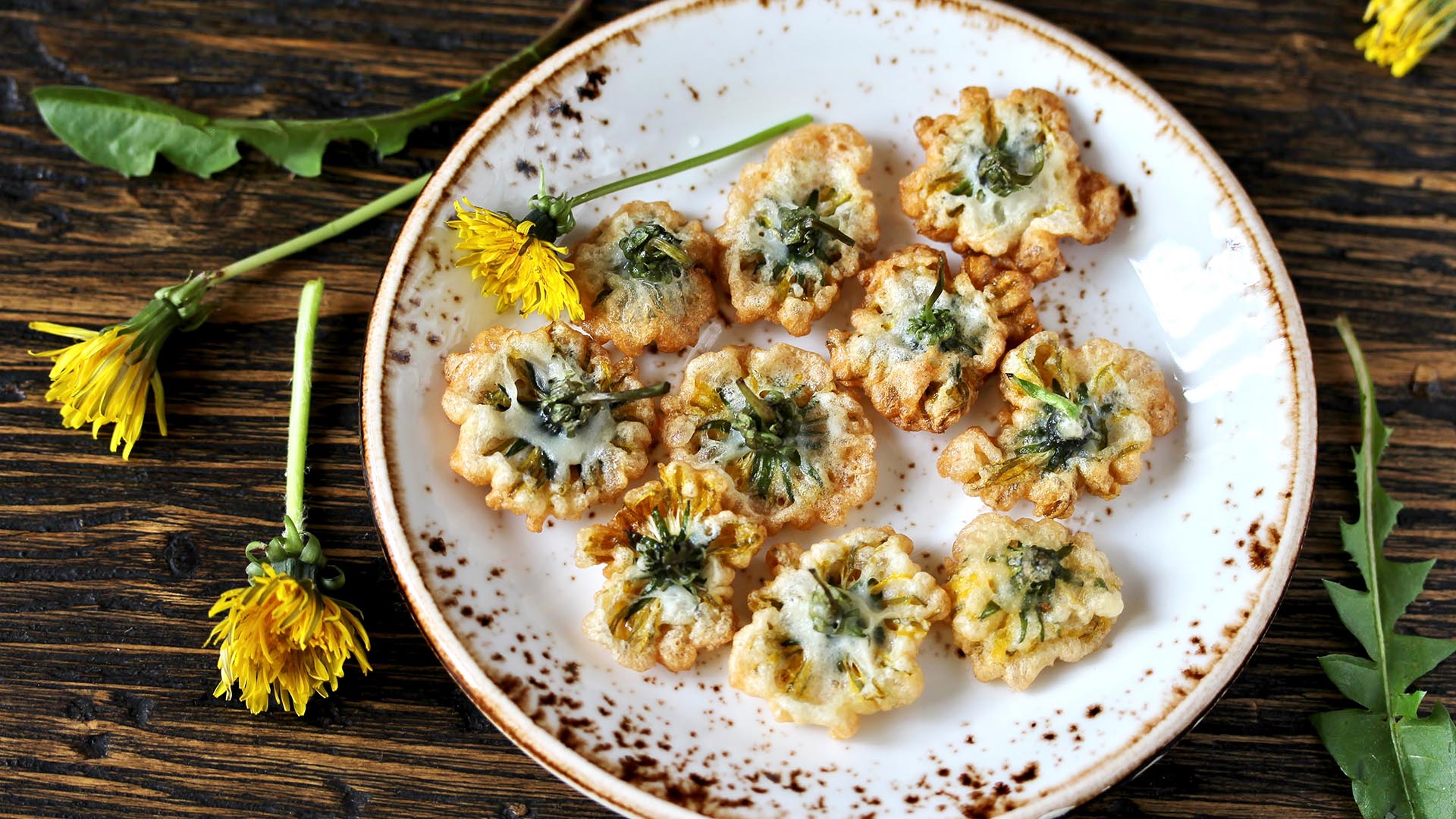 Overhead view of white, round plate with fried dandelions on a wooden service. 