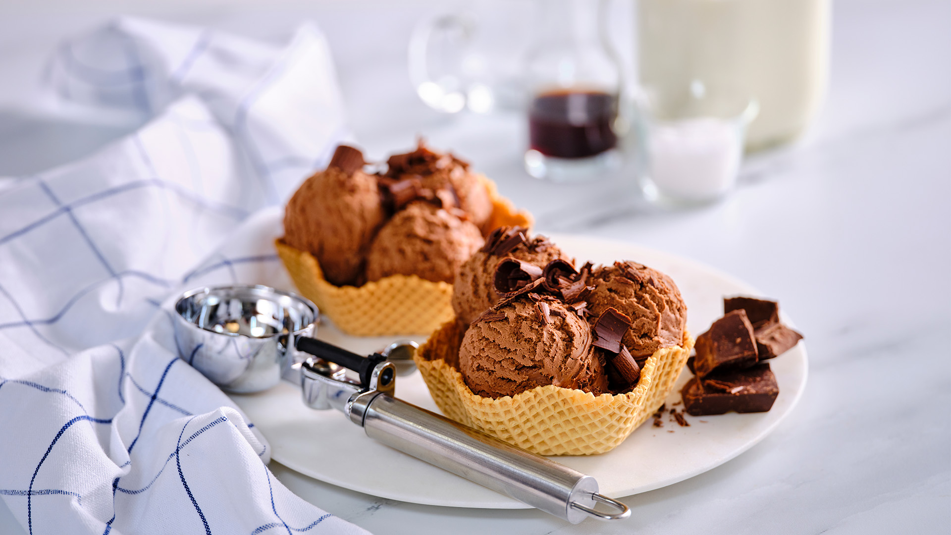Two waffle cone bowls with scoops of chocolate ice cream with chocolate shavings on top. 