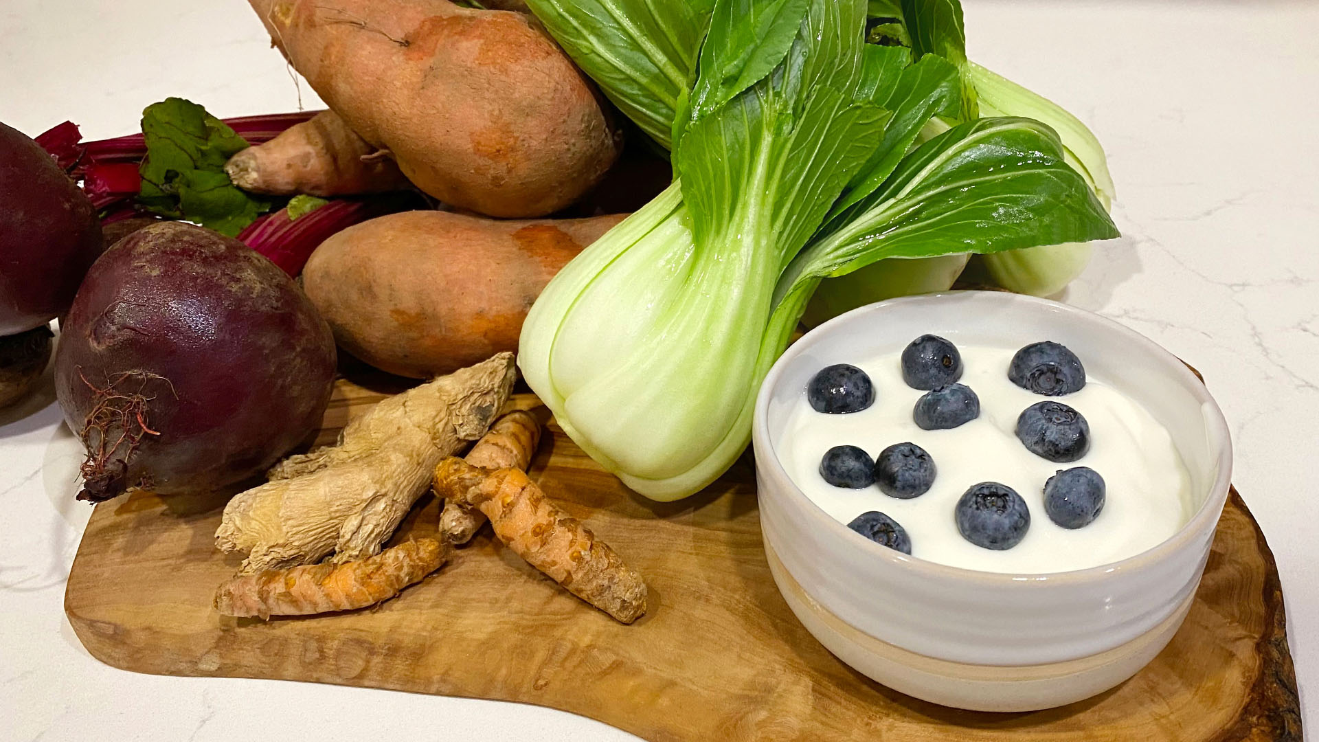 A wooden board with vegetables and a bowl of yogurt with blueberries.