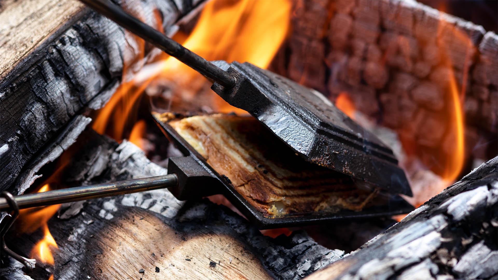 Black pie iron slightly open in a campfire.