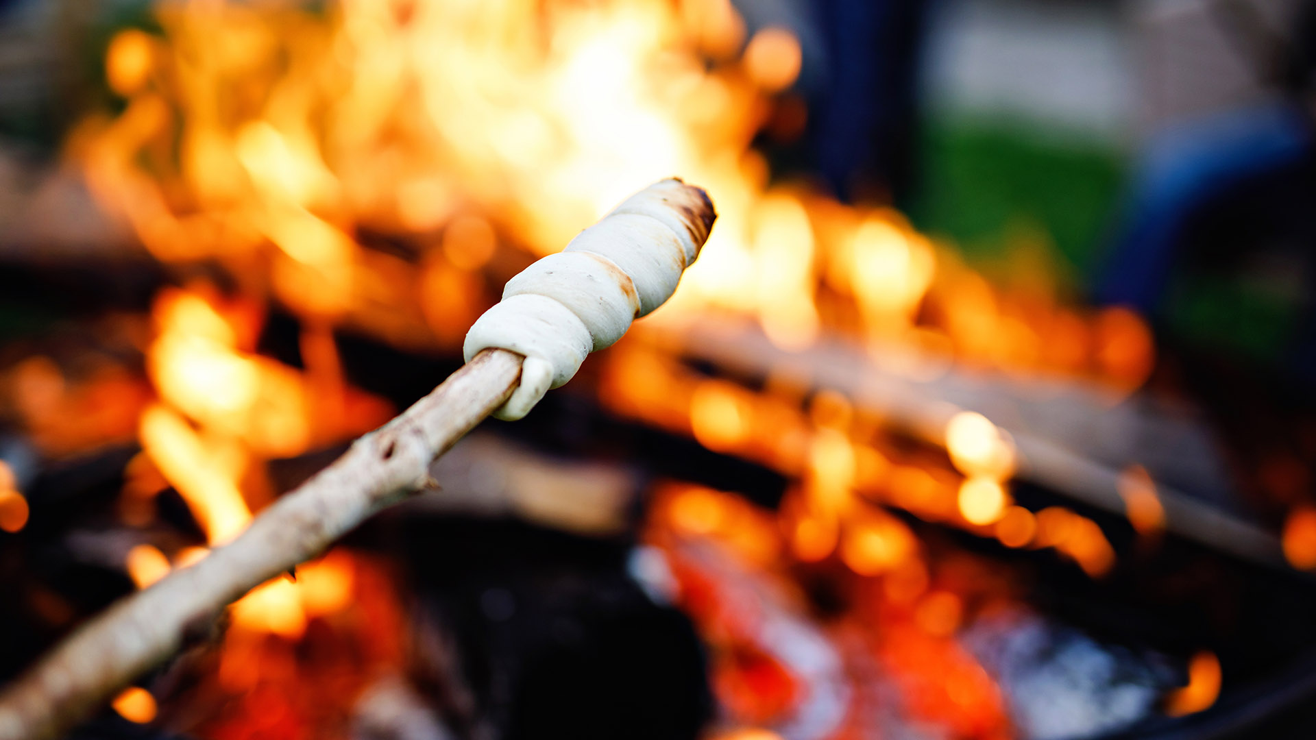A stick with some dough wrapped on the end end roasting over a campfire.