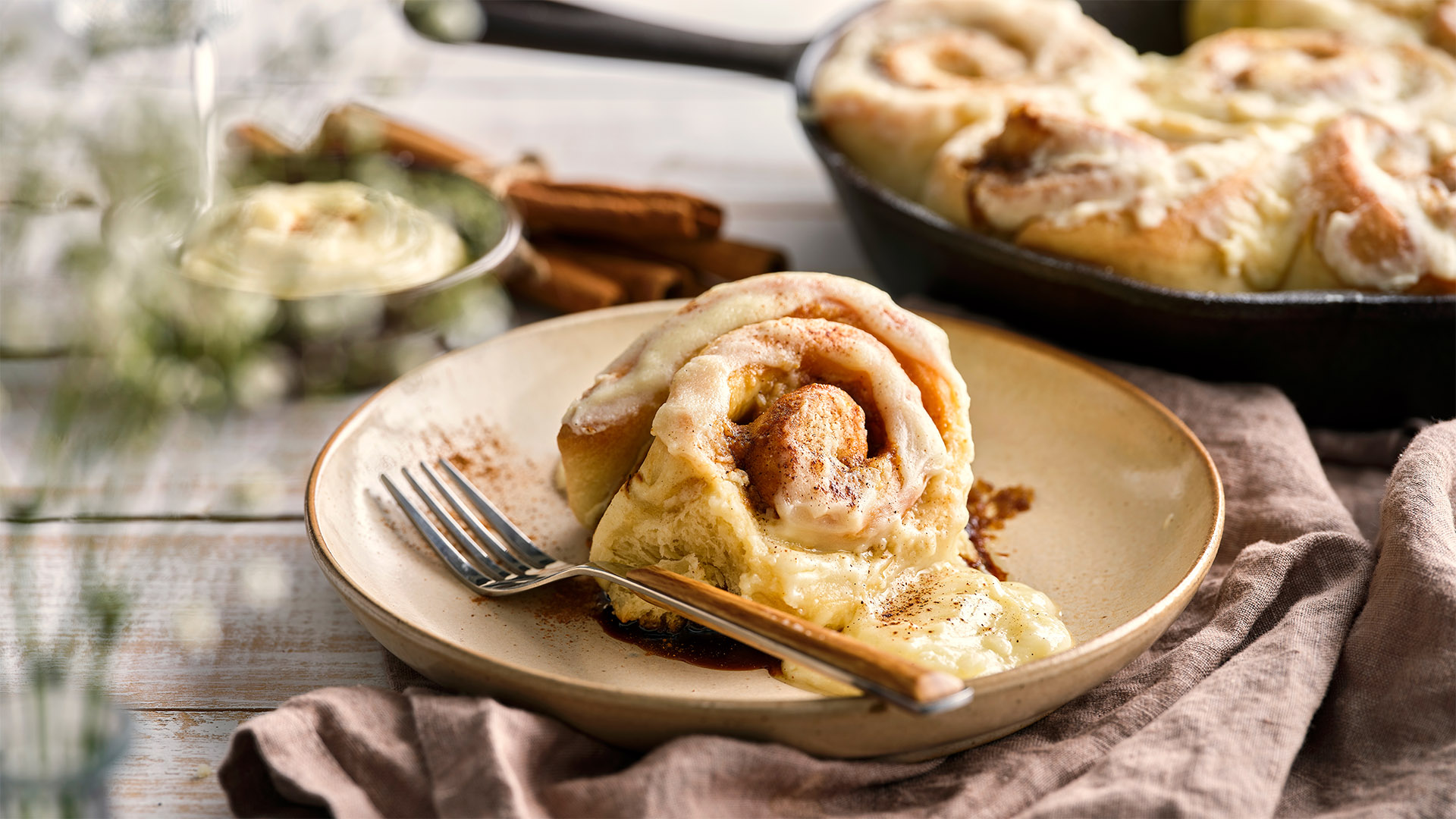 A cast iron pan is filled with Mascarpone Brioche Cinnamon Rolls and sits next to a plate with a serving.
