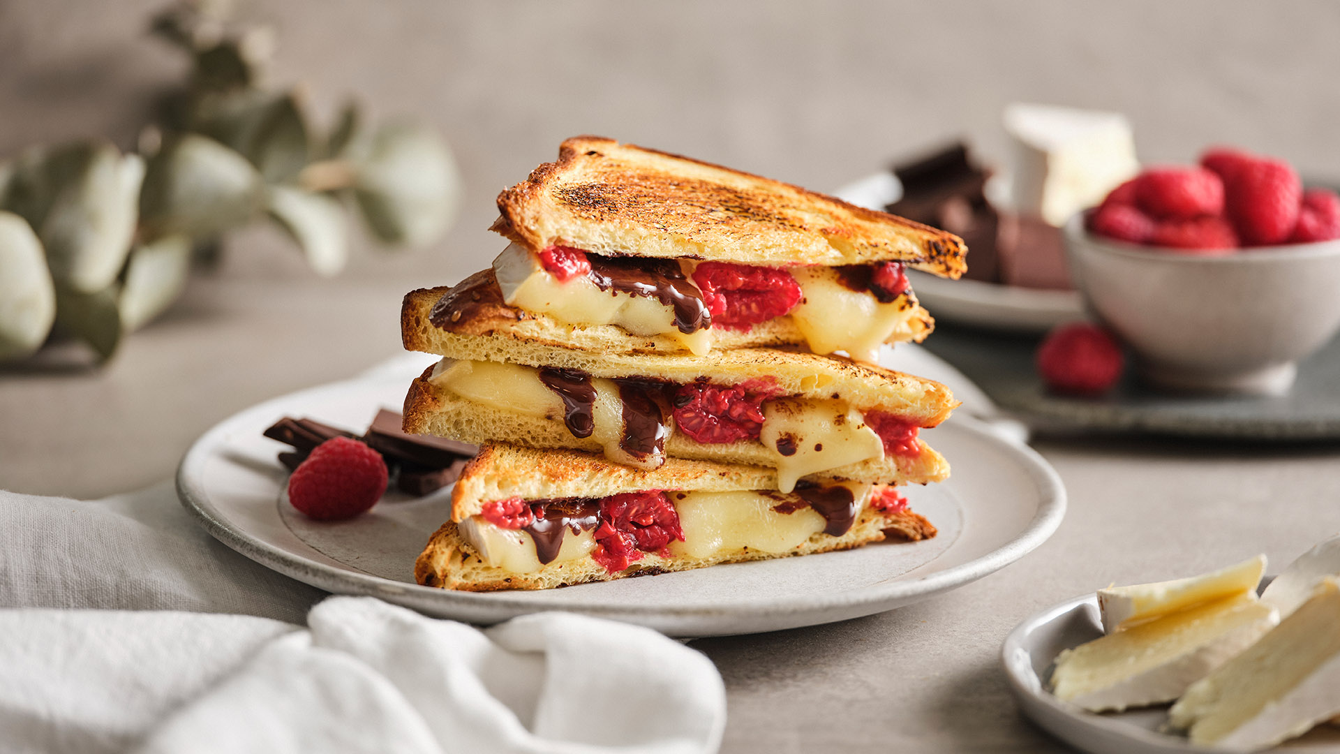 A stack of four brie, dark chocolate, and raspberry grilled cheese sandwiches on a round, light coloured plate. 