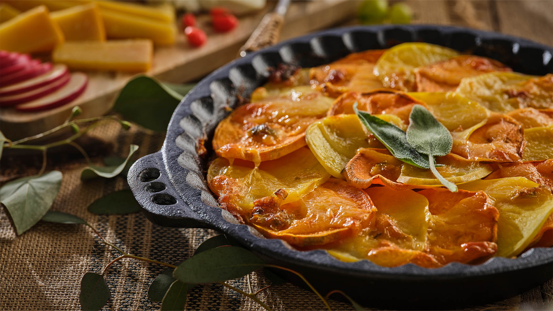 Double Scalloped Potatoes with Aged Ontario Gouda in a round, black cast iron dish with handles topped with fresh sage leaves. 
