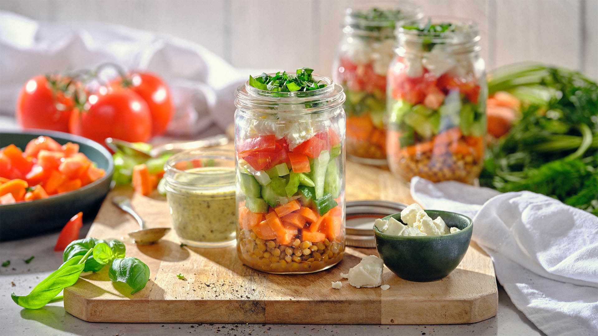 Side shot of jar filled with salad ingredients on a wooden board surrounded by salad ingredients and toppings.