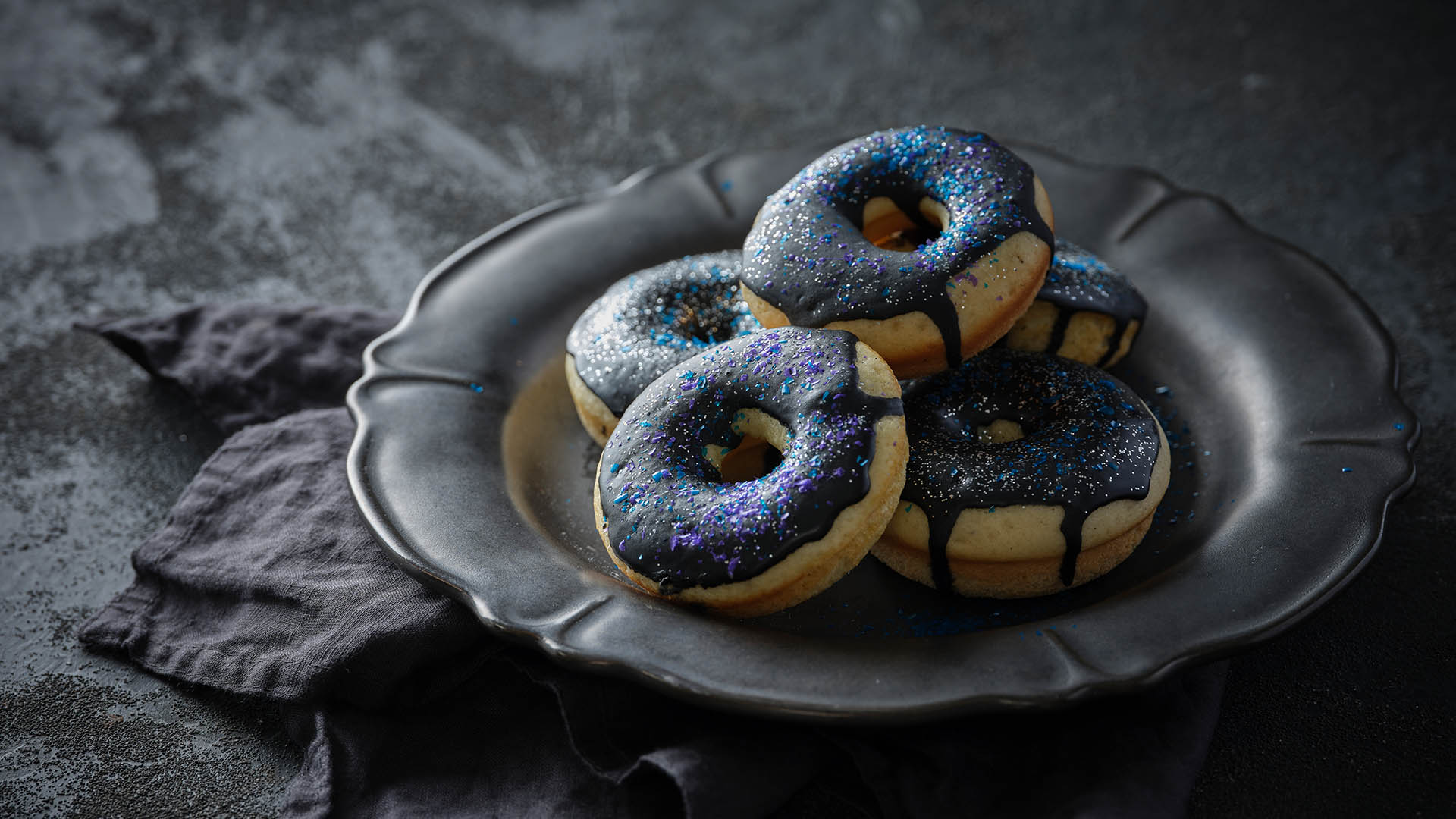 Side shot of Kefir donuts with dark sparkly glaze on a black plate.