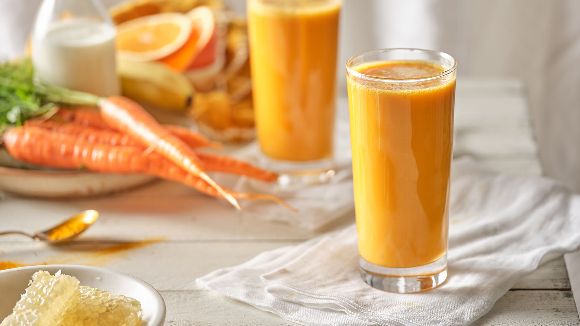 Two glasses with orange Kefir smoothie with pitcher of milk and carrots in the background.