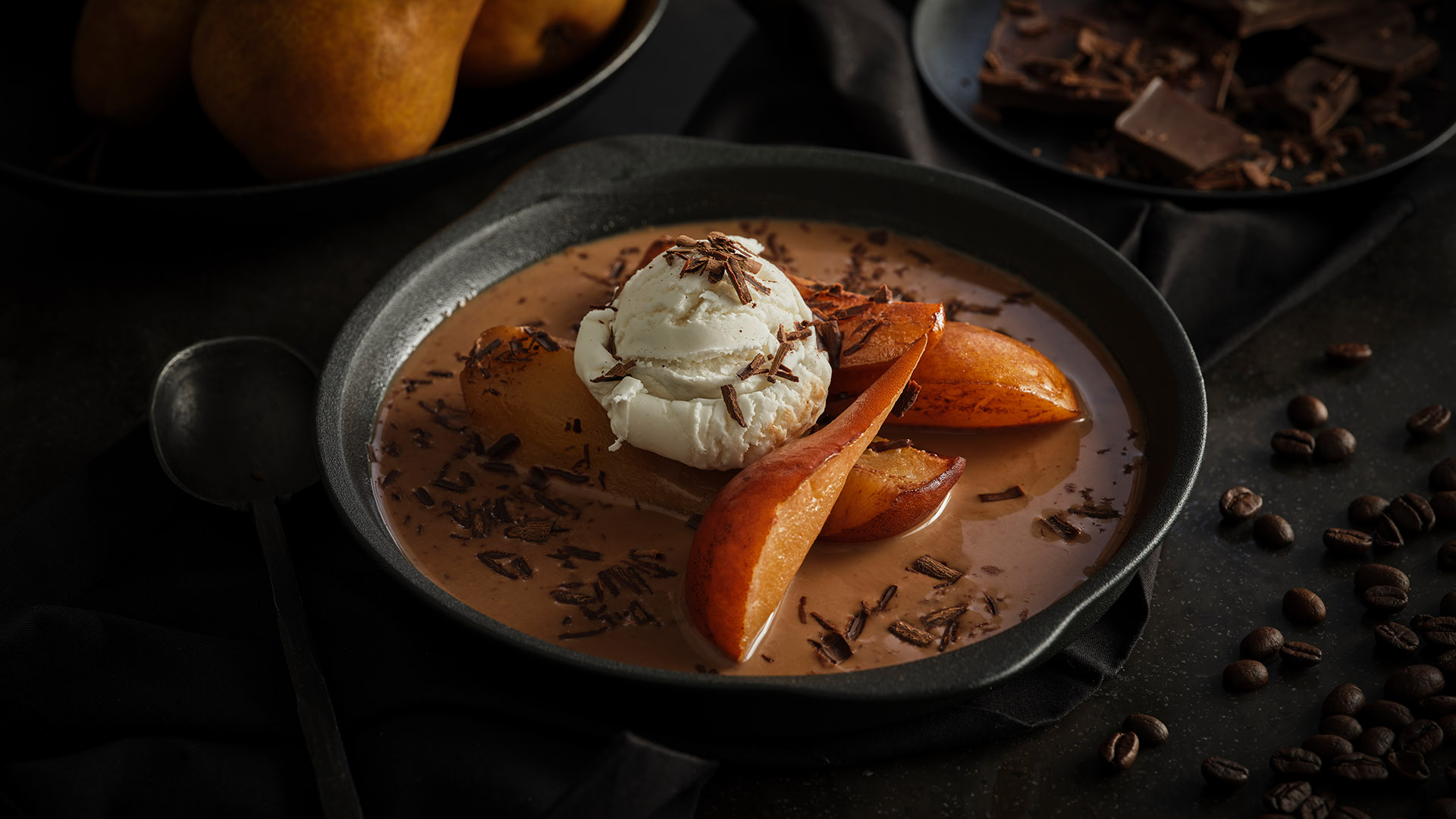 Slow cooked mocha poached pears with a dollop of ice cream on top in a round black bowl. 