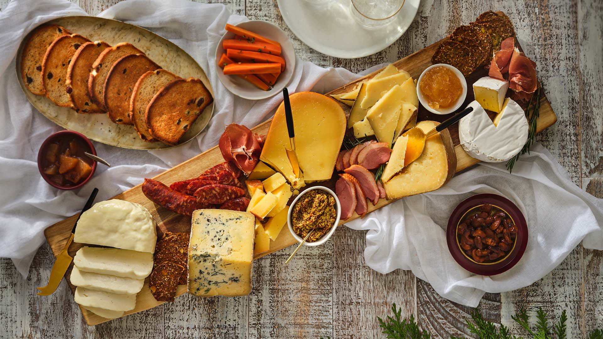 Overhead view of a cheese board with various types of artisanal cheeses, meats, and jelly and mustard spread.