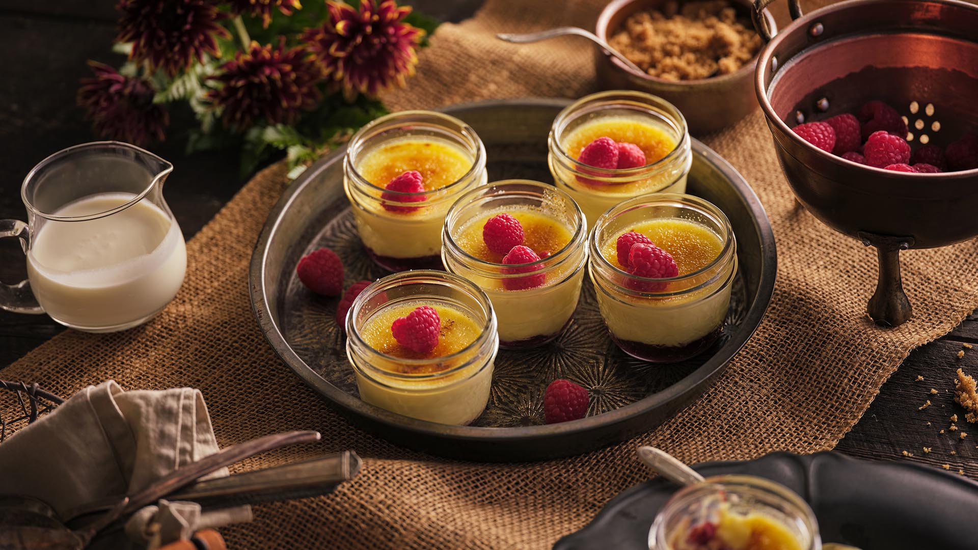 Five small jars with creme brûlée on round metal serving tray.