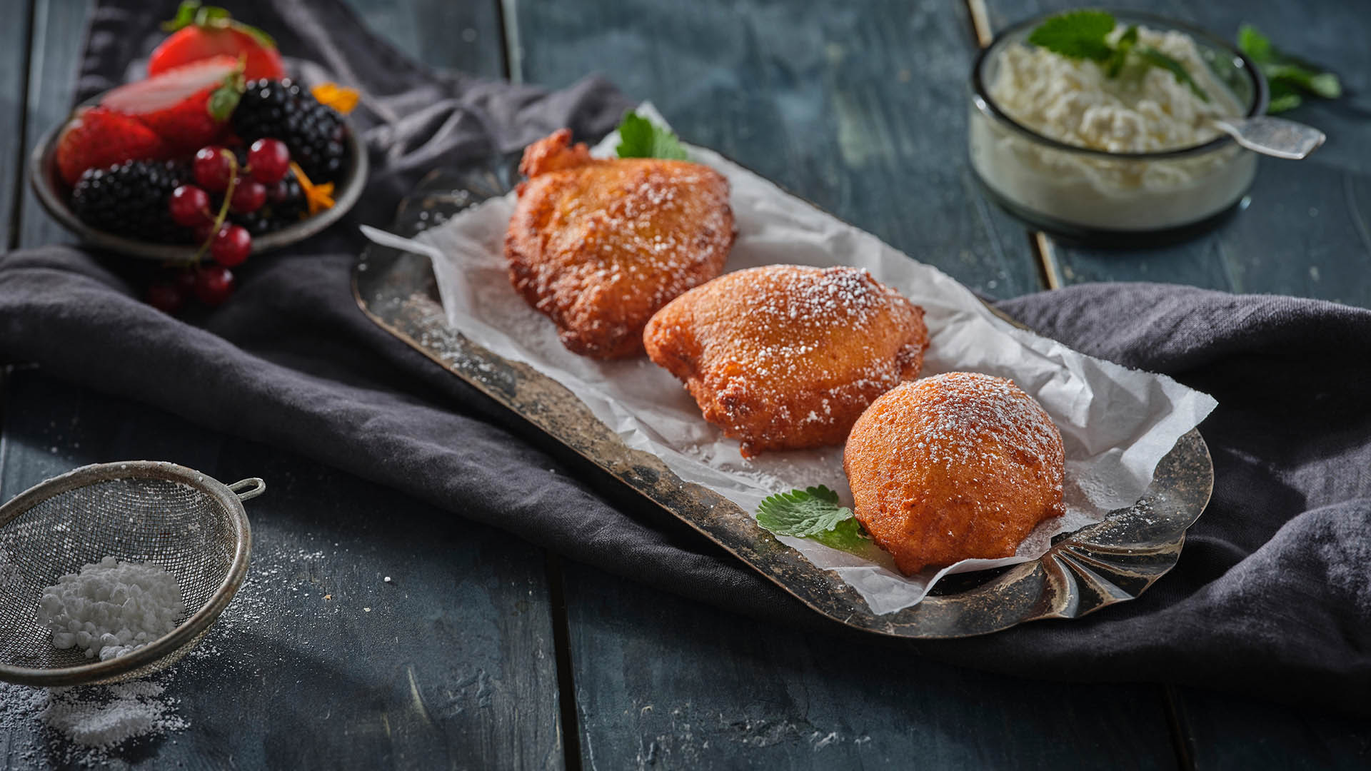 Three ricotta fritters on top of parchment paper on small rectangular serving board.
