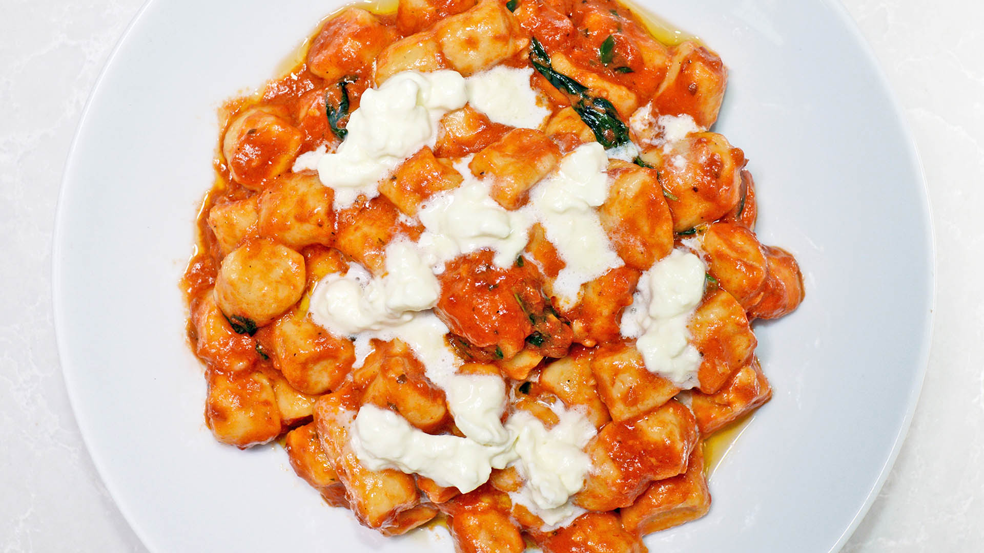 Overhead shot of gnocchi with tomato sauce in round white pasta bowl.