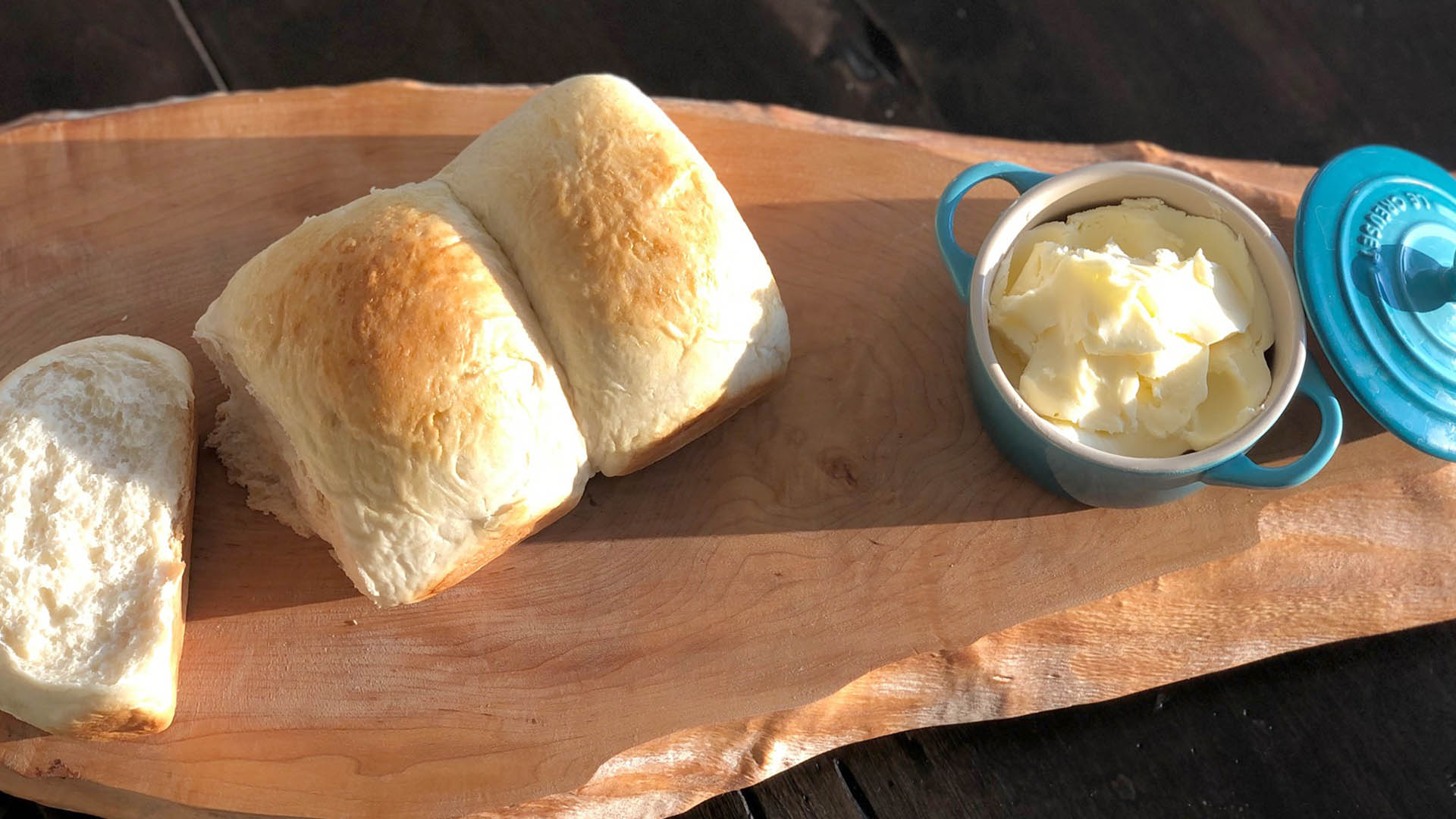 Overhead shot of three pieces of milk bread with small blue dish filled with honey butter on wooden serving board.