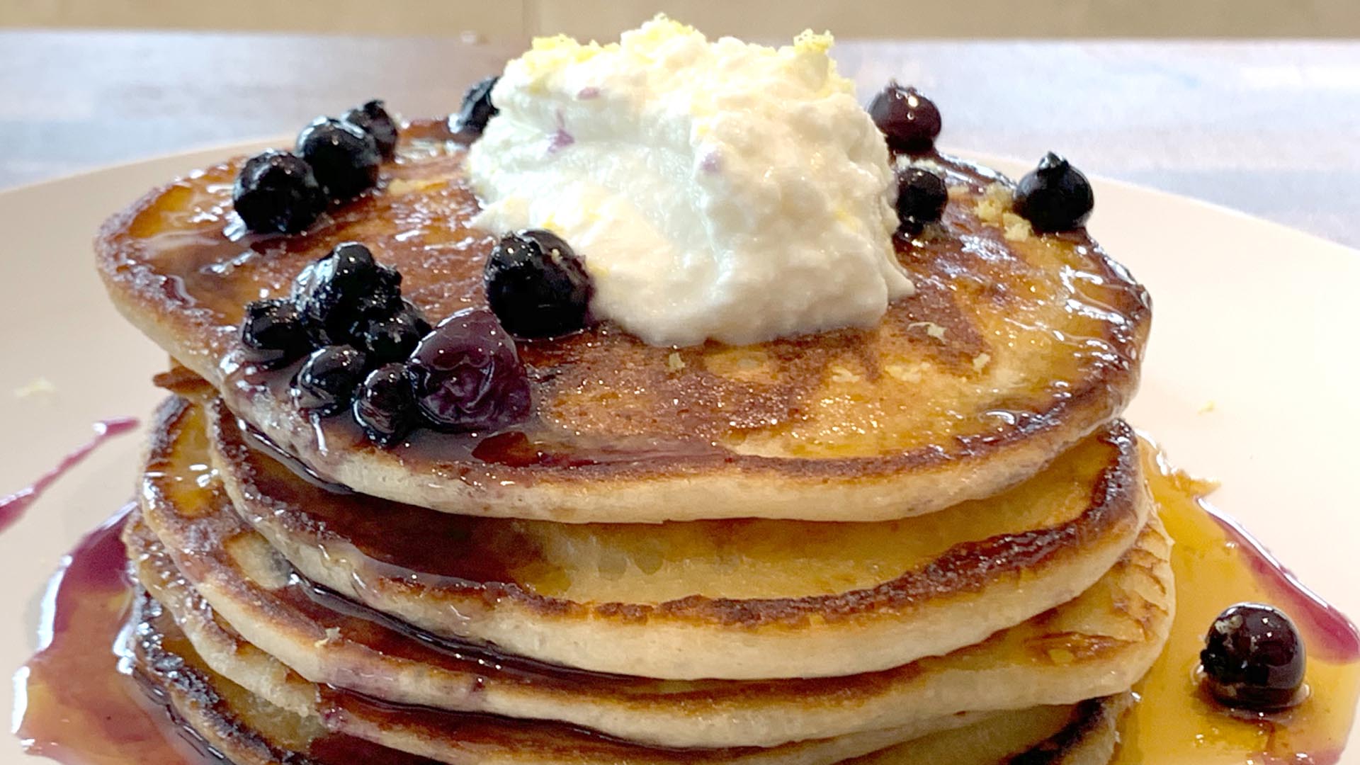 Stack of pancakes with berry drizzle on white round plate.
