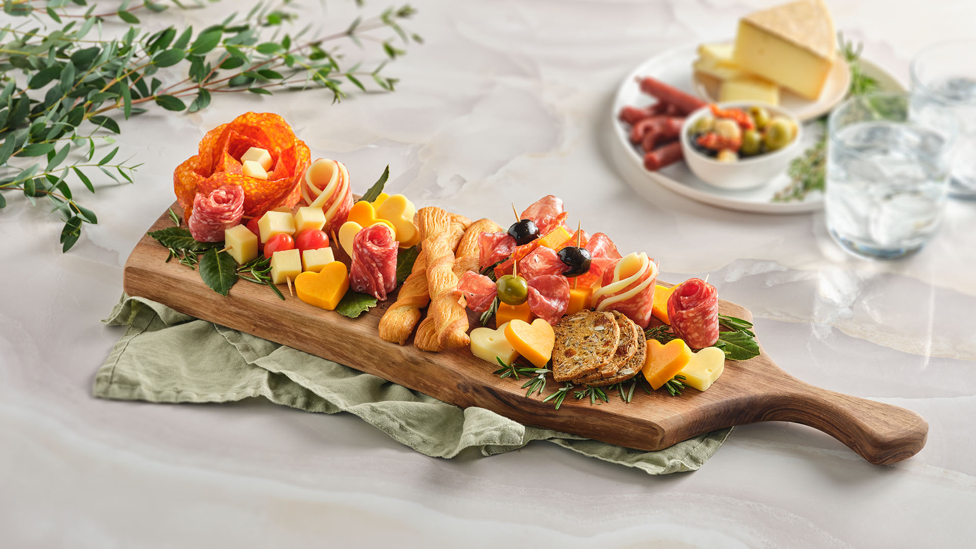 A rectangular, wooden board with assorted artisanal cheeses and meats, the board is on top of a light green napkin.